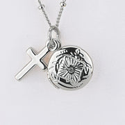 Silver necklace with a cross pendant and round locket on a light gray background