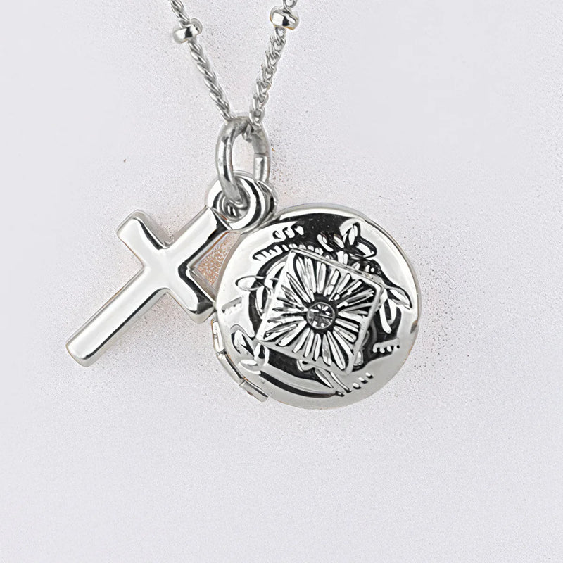 Silver necklace with a cross pendant and round locket on a light gray background