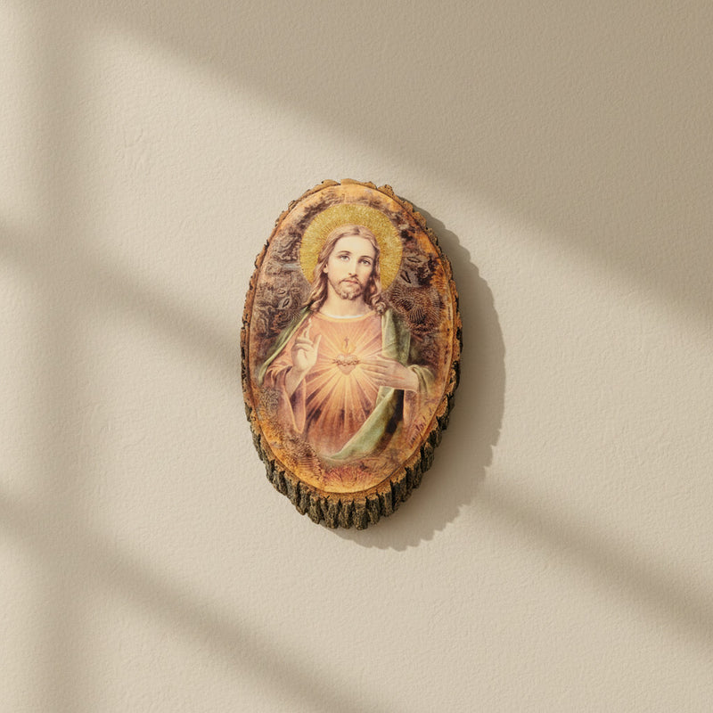 Oval-shaped, rustic wall plaque of the Sacred Heart of Jesus on a beige wall in midday lighting.