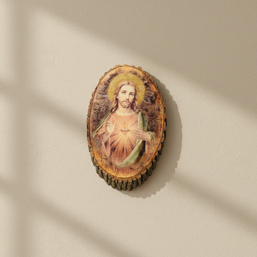 Oval-shaped, rustic wall plaque of the Sacred Heart of Jesus on a beige wall in midday lighting.