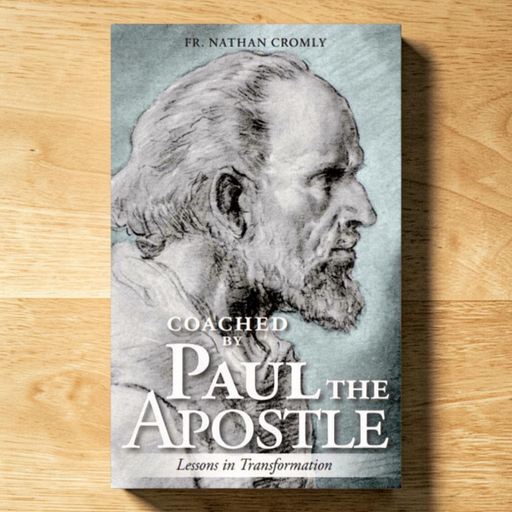 A book titled "Coached by Paul the Apostle: Lessons in Transformation" by Fr. Nathan Cromly, featuring a grayscale portrait sketch on a muted blue-gray cover, photographed standing upright on a light wood surface.