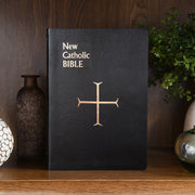 Black New Catholic Bible with gold text and cross symbol on a wood background.