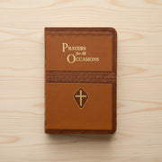 Brown prayer book with 'Prayers for All Occasions' text and cross emblem on a pine wood background