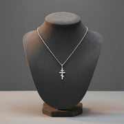 Silver necklace with a cross pendant on a black mannequin bust against a gray background