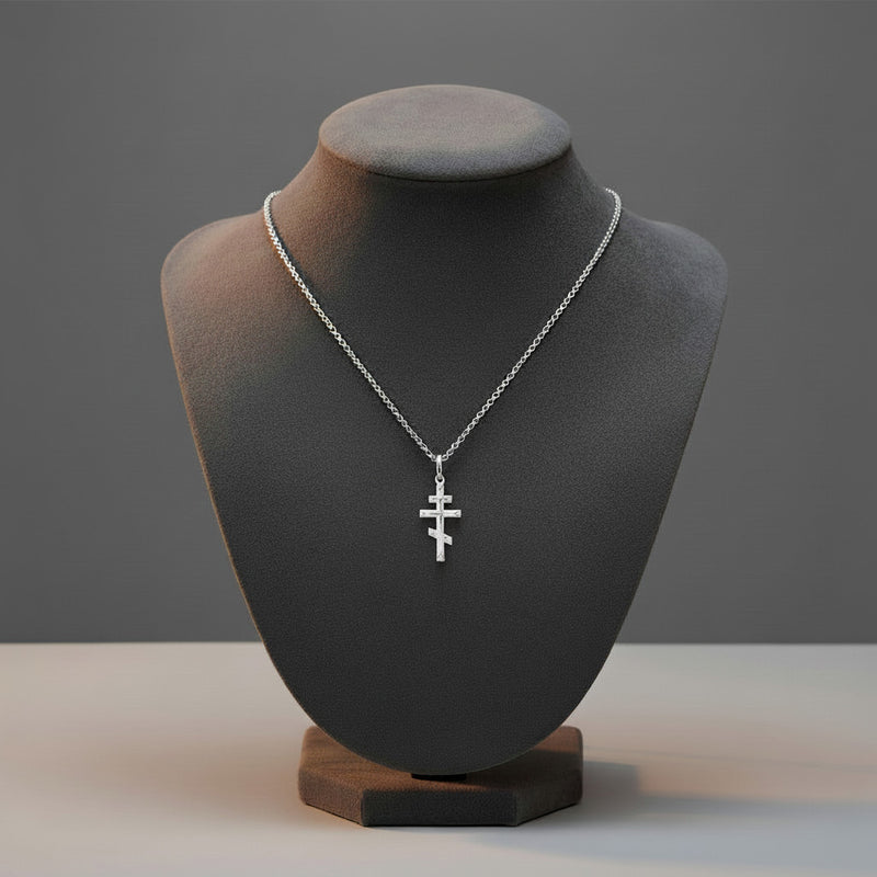 Silver necklace with a cross pendant on a black mannequin bust against a gray background