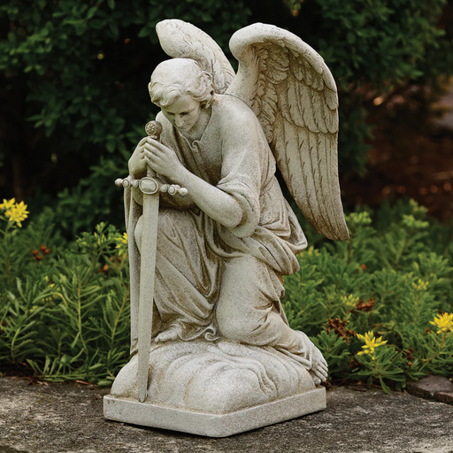 Outdoor statue of a male angel kneeling in prayer with a sword in a garden background.