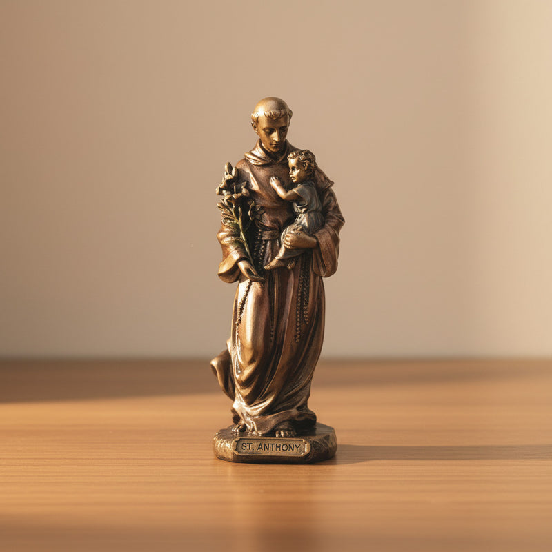 Bronze statue of St. Anthony of Padua holding the Divine Child on a wooden surface with a beige background