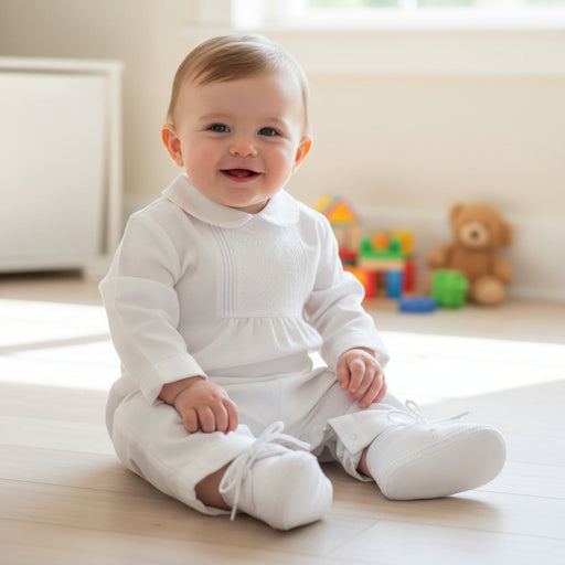 Baby in a white outfit sitting on a wooden floor with toys in the background
