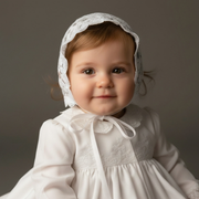 Baby in a white baptism cap sitting on a gray background