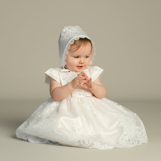 Baby in a white lace baptism dress and bonnet on a plain background