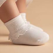 White baptismal sock with lace trim on a beige background