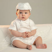Baby in a white baptism outfit with a hat sitting on a light-colored surface