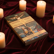 A book titled 'Behold My Heart' lying on a red velvet background amid candles
