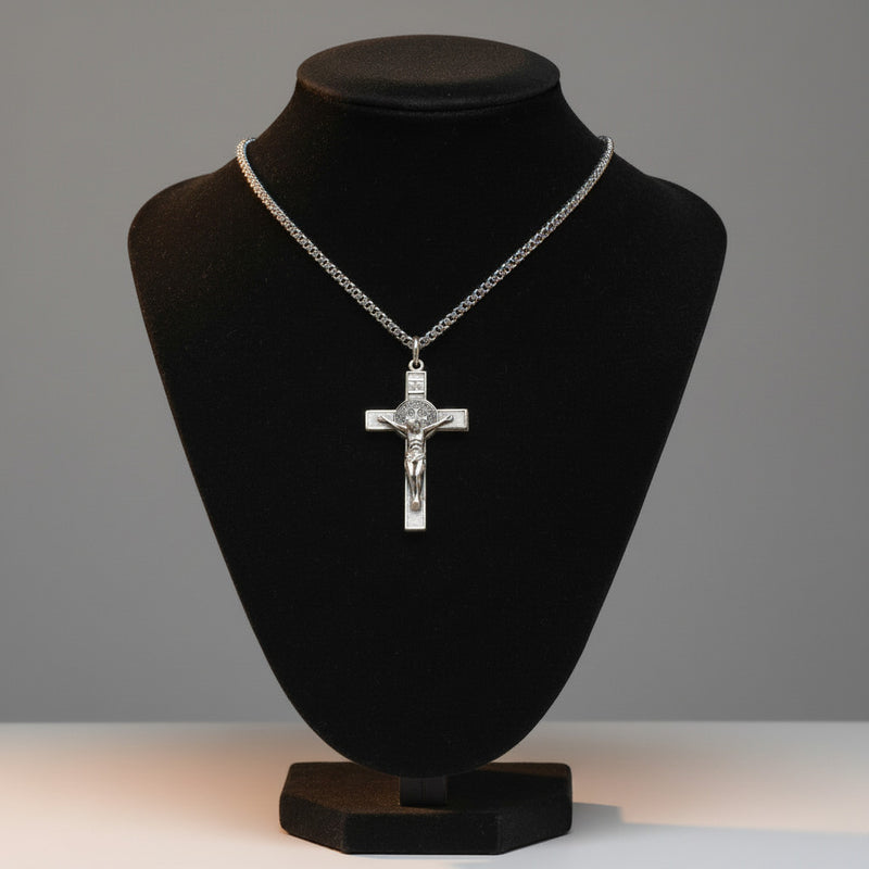 Silver crucifix necklace on a black velvet bust against a gray background