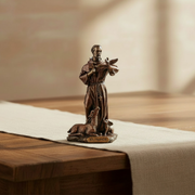 Miniature bronze figurine of St. Francis of Assisi on a wood table.