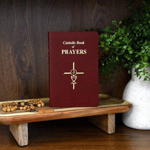 Catholic Book of Prayers on a wooden stand with a rosary and plant in the background
