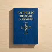 Blue book titled 'Catholic Treasury of Prayers' with a gold cross on a wooden surface
