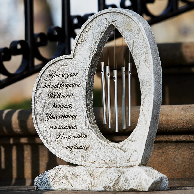 Heart-shaped stone sculpture with engraved text and metal chimes on a blurred background