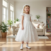 Young girl in a white lace dress standing in a bright living room.