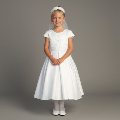 Young girl wearing a white Communion dress with a veil against a gray background