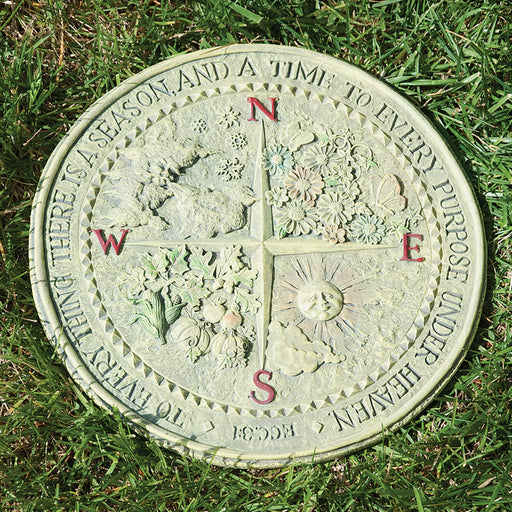 Decorative compass stone with floral designs and text on grass
