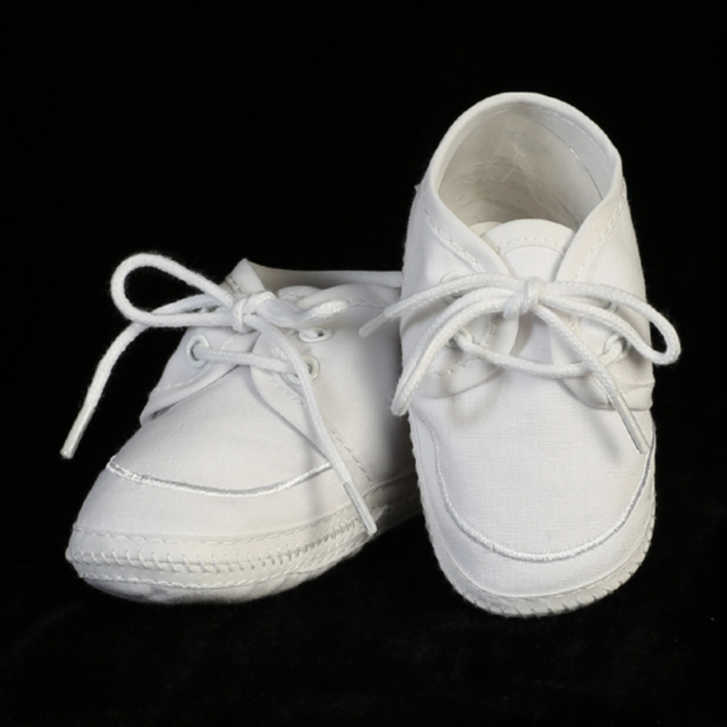 Pair of white baby shoes with laces on a black background