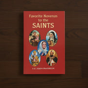Red prayerbook titled 'Favorite Novenas to the Saints' with images of saints on a wooden surface