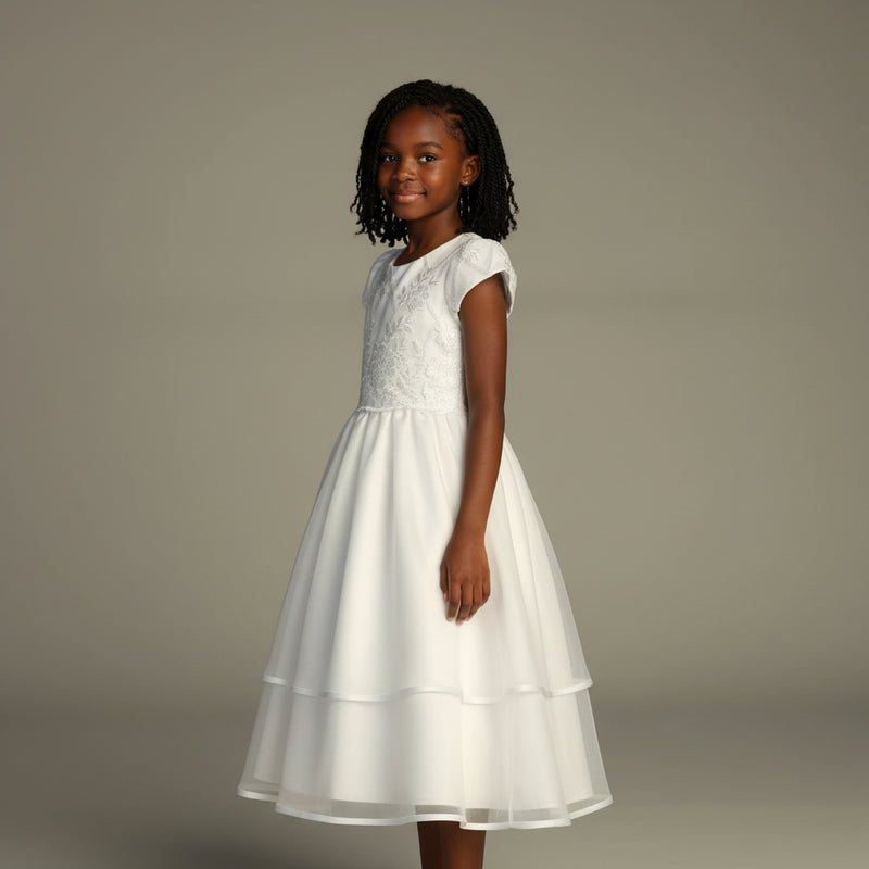 Young girl wearing a white communion dress against a plain background
