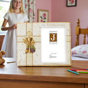 First Communion gift 3.5 x 5 inch photo frame featuring a decorative gold chalice design, with a photo of the 'Joseph's Studio' brand logo, sitting on a wooden desk, with a little girl in the background.