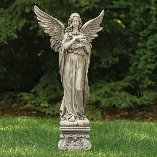 Statue of an angel holding flowers on a grassy area with trees in the background