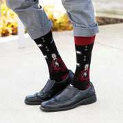 Person wearing black Fulton Sheen socks with red accents on a light gray pavement.