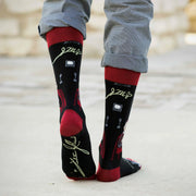 Person wearing black Fulton Sheen socks with red accents on a light gray pavement.
