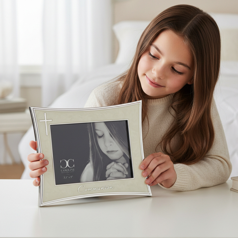 Young girl holding an ivory and silver First Communion picture frame for a 3.5 x 5 inch size photo in a bedroom setting.