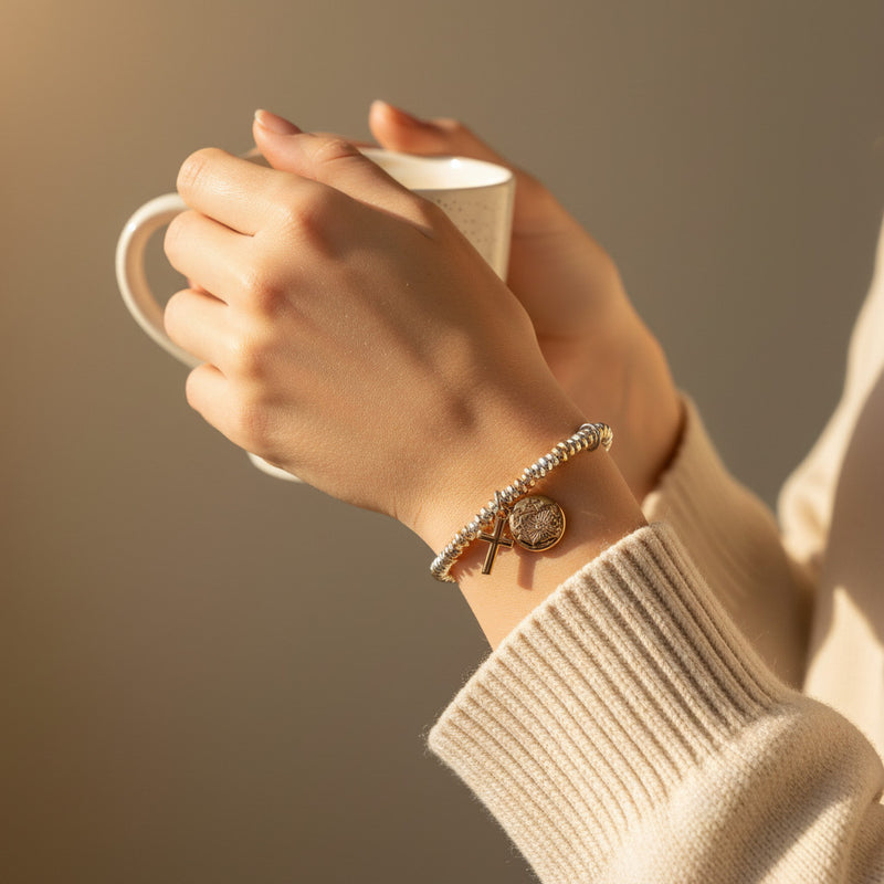 Hand holding a mug with a wrist wearing a bracelet against a warm background