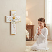 Young girl in kneeling and praying in a room with a decorative First Communion cross gift on the wall.