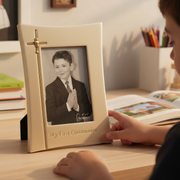 Decorative First Communion gift picture frame sits on a little boy's desk, with a 4x6 inch black and white photo of a boy in a suit with hands folded in prayer.