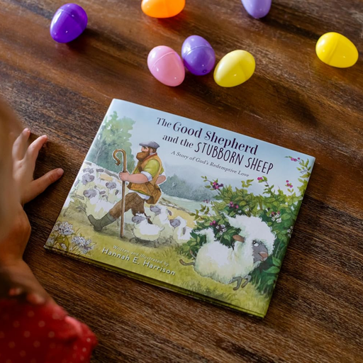 Children's book titled 'The Good Shepherd and the Stubborn Sheep' on a wooden surface with colorful Easter eggs.