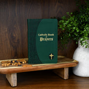 Green Catholic Book of Prayers on a wooden stand with a plant in the background