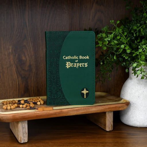 Green Catholic Book of Prayers on a wooden stand with a plant in the background
