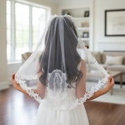 Girl wearing a white Communion dress with a lace Our Lady of Guadalupe veil indoors.
