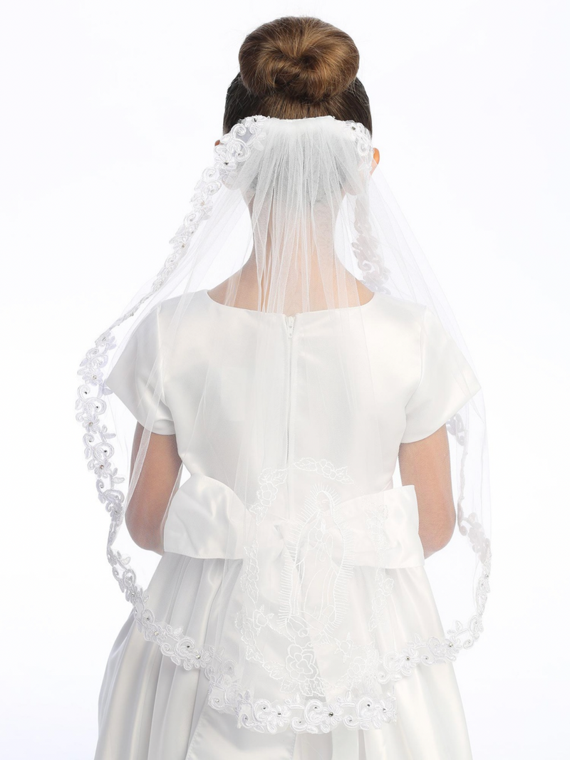 A girl wearing a white communion veil with corded lace trim, featuring an image of Our Lady of Guadalupe on the back.