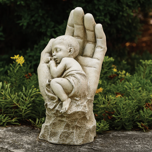 Statue of a hand holding a sleeping baby with a garden background
