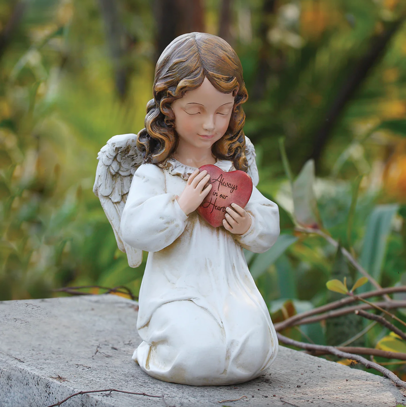 Angel figurine holding a heart, kneeling on a rock with a natural background