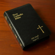 Black New Catholic Bible with gold text and cross on a wooden surface