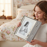 Young girl holding a boxed picture frame for a 4x6 inch photo and a rosary in a bedroom setting