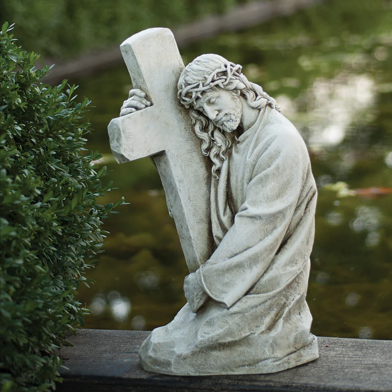Outdoor statue of Jesus embracing the cross in a backyard setting.
