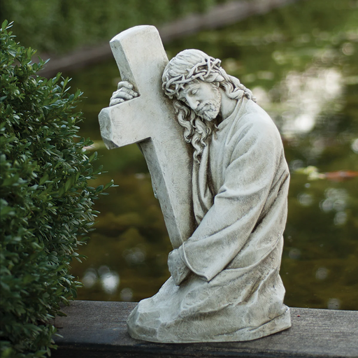 Outdoor statue of Jesus embracing the cross in a backyard setting.