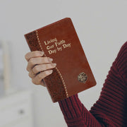 Brown leather book titled 'Living Our Faith Day by Day' held by a person wearing a red sweater.