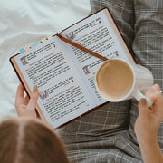 Person reading a prayer book with a mug of coffee on a bed