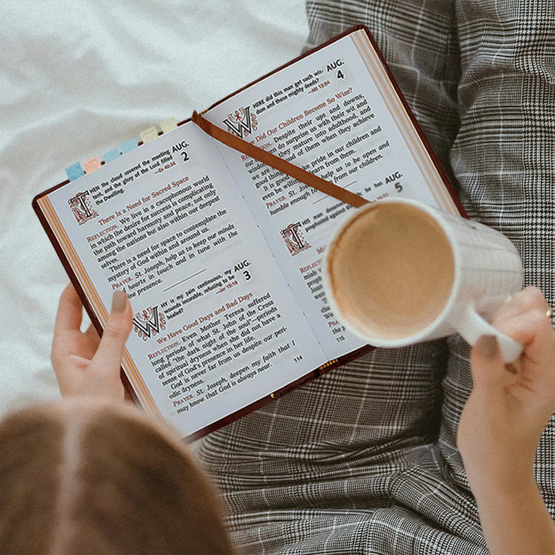 Person reading a prayer book with a mug of coffee on a bed